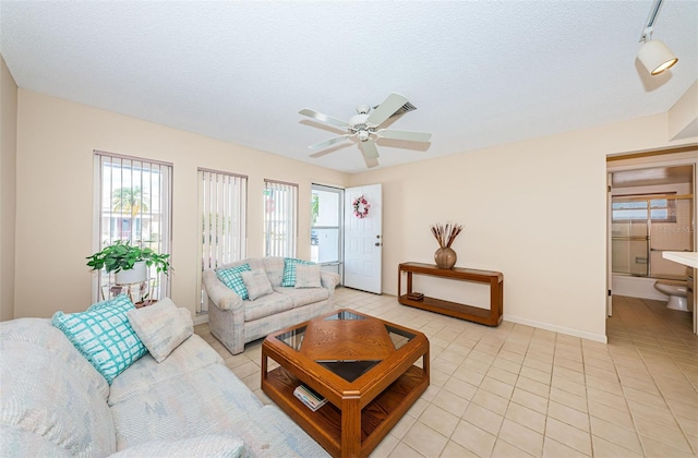 living area featuring ceiling fan, a textured ceiling, baseboards, and light tile patterned floors