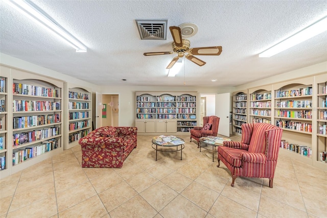 sitting room with a textured ceiling, light tile patterned floors, wall of books, and visible vents