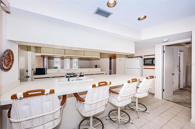 kitchen with light countertops, a breakfast bar, a peninsula, and freestanding refrigerator