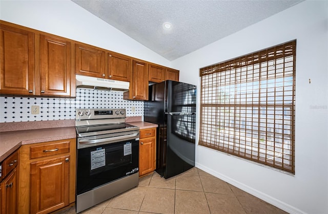 kitchen with a textured ceiling, lofted ceiling, stainless steel electric stove, black refrigerator, and light tile patterned floors