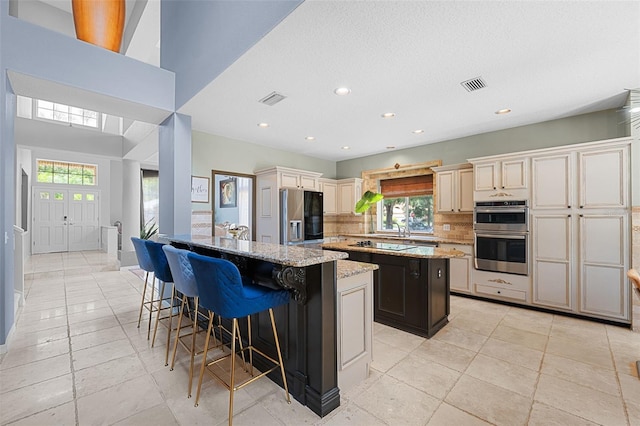 kitchen with a center island, cream cabinets, decorative backsplash, light stone countertops, and stainless steel appliances