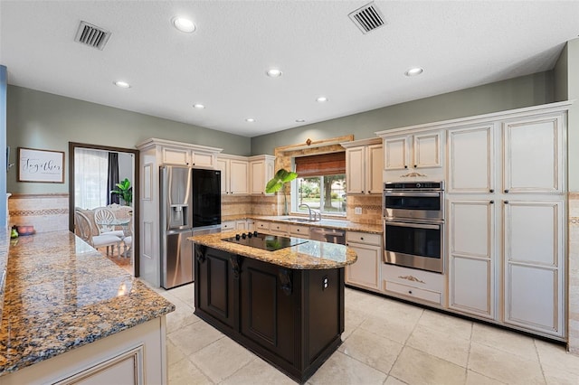 kitchen featuring light stone countertops, appliances with stainless steel finishes, tasteful backsplash, cream cabinetry, and a kitchen island