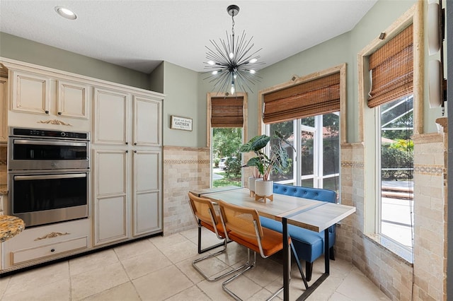 kitchen with double oven, cream cabinets, a chandelier, decorative light fixtures, and tile walls