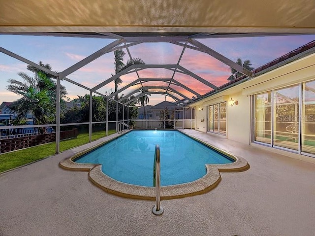 pool at dusk with glass enclosure and a patio area