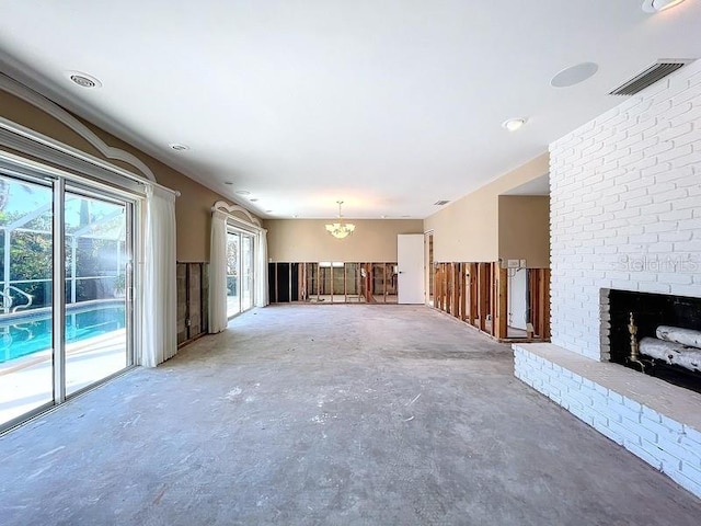 unfurnished living room featuring a chandelier, concrete floors, and a brick fireplace