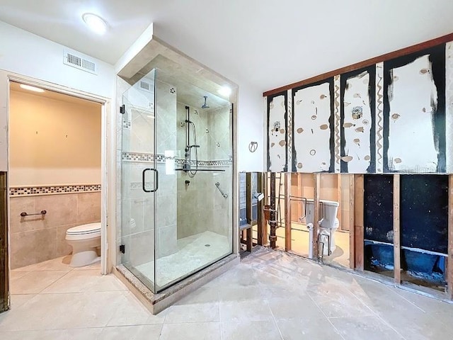 bathroom featuring tile patterned floors, a shower with door, toilet, and tile walls