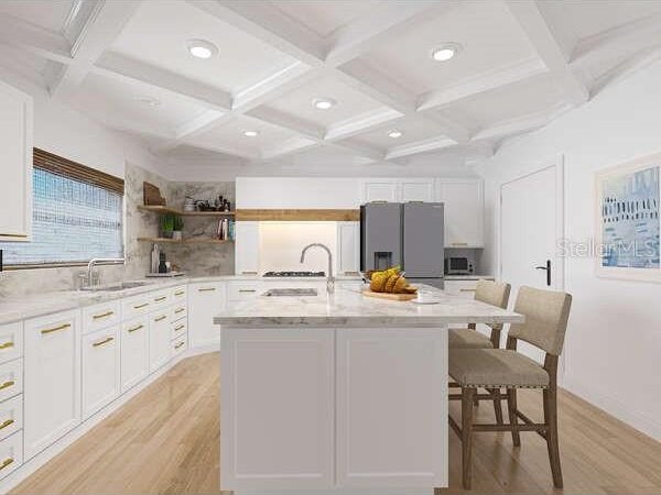 kitchen featuring white cabinetry, stainless steel appliances, an island with sink, decorative backsplash, and light wood-type flooring