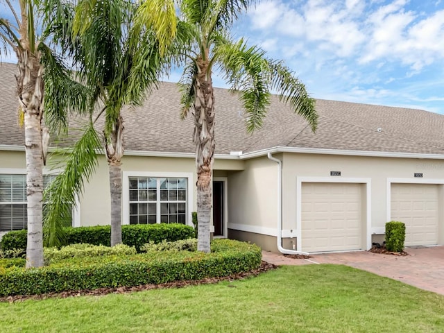 multi unit property with a shingled roof, decorative driveway, a front lawn, and stucco siding