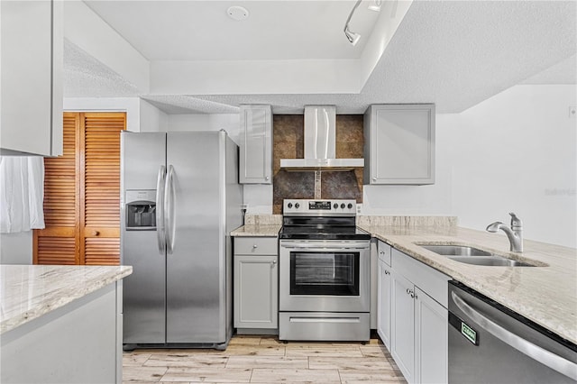 kitchen with sink, wall chimney exhaust hood, light wood-type flooring, a textured ceiling, and stainless steel appliances