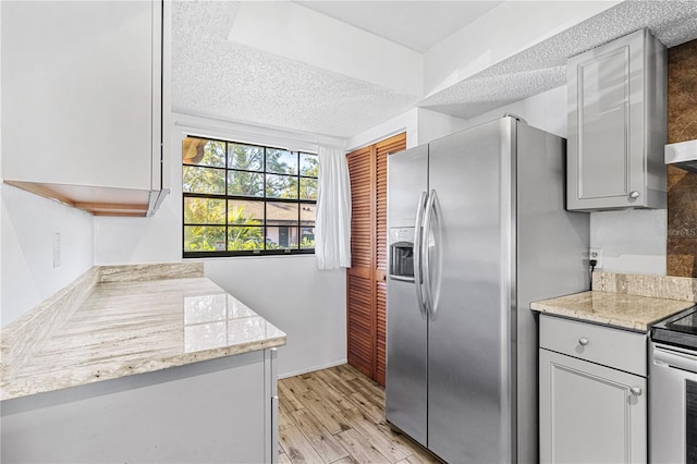 kitchen with gray cabinets, light stone countertops, a textured ceiling, light hardwood / wood-style floors, and stainless steel appliances