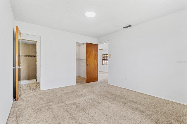 unfurnished bedroom featuring carpet flooring, a spacious closet, a textured ceiling, and a closet