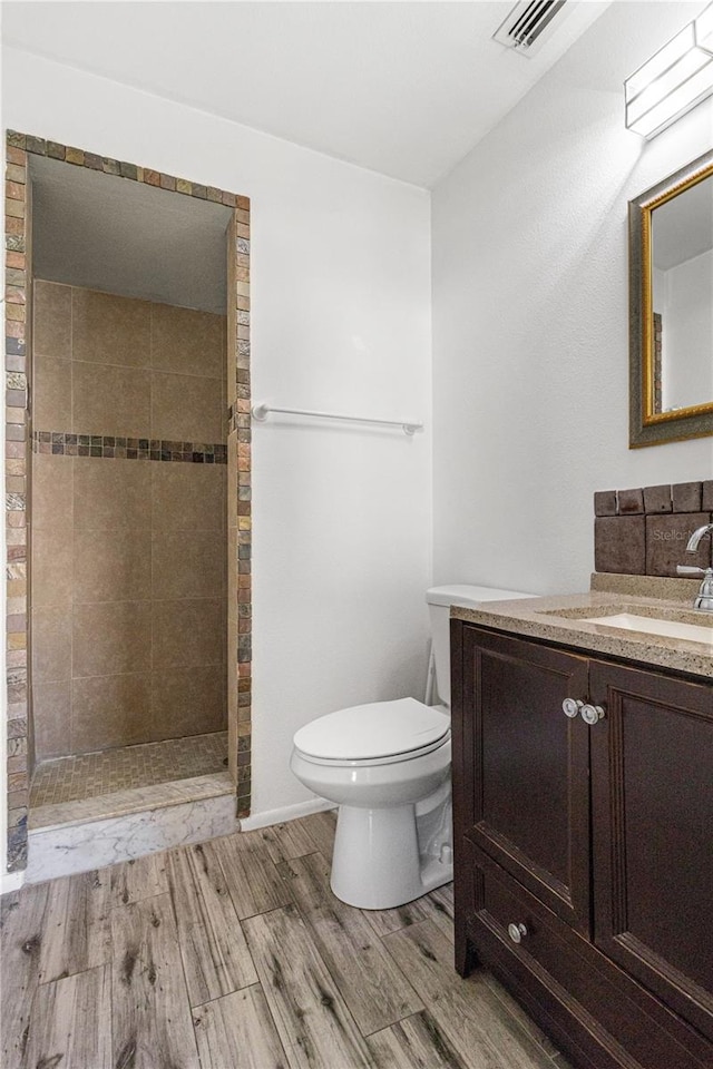 bathroom featuring a tile shower, vanity, wood-type flooring, and toilet