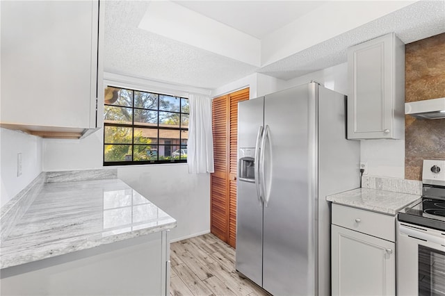 kitchen featuring light wood finished floors, light stone counters, appliances with stainless steel finishes, a textured ceiling, and wall chimney range hood