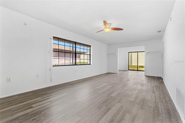 spare room featuring a textured ceiling, wood finished floors, visible vents, and a ceiling fan