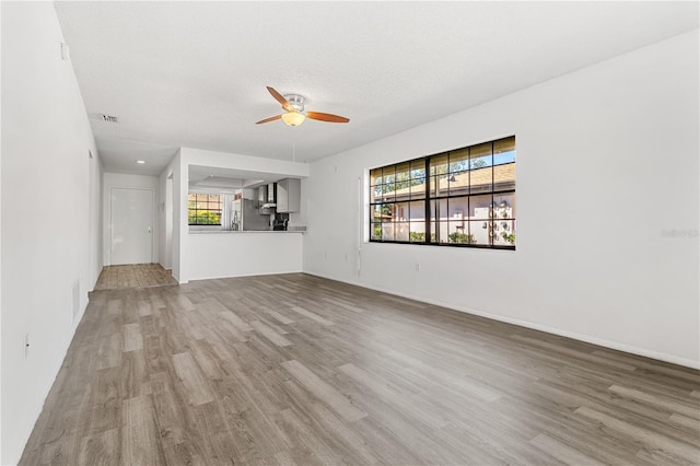 unfurnished living room with a healthy amount of sunlight, visible vents, a ceiling fan, and wood finished floors