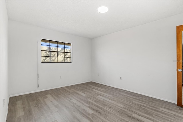 empty room with a textured ceiling, light wood finished floors, and baseboards