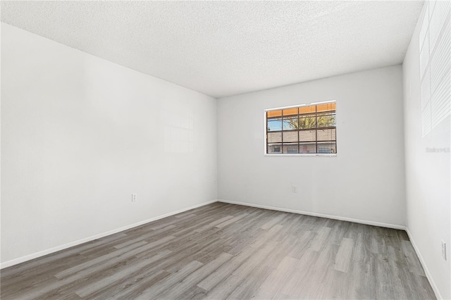 unfurnished room with a textured ceiling, baseboards, and wood finished floors