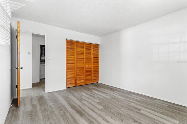 unfurnished bedroom with washer / clothes dryer, a closet, a textured ceiling, wood finished floors, and baseboards