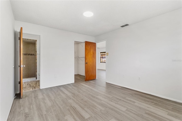 unfurnished bedroom with baseboards, a closet, light wood-type flooring, a walk in closet, and ensuite bath