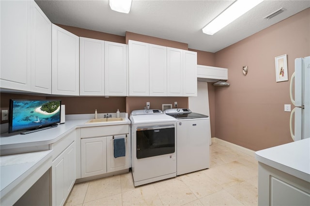 washroom with a textured ceiling, cabinets, separate washer and dryer, and sink