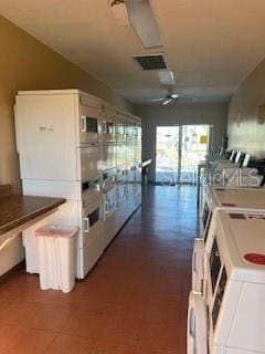 kitchen featuring stacked washer / dryer, ceiling fan, and white cabinets