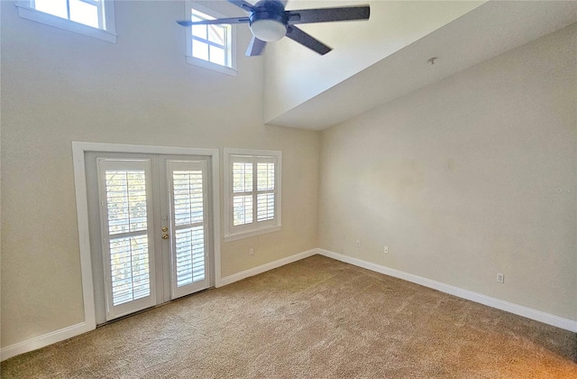 carpeted empty room with ceiling fan, a high ceiling, and french doors