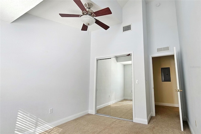 unfurnished bedroom featuring ceiling fan, a closet, light colored carpet, and a high ceiling