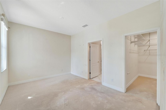 unfurnished bedroom featuring multiple windows, a walk in closet, light colored carpet, and a closet