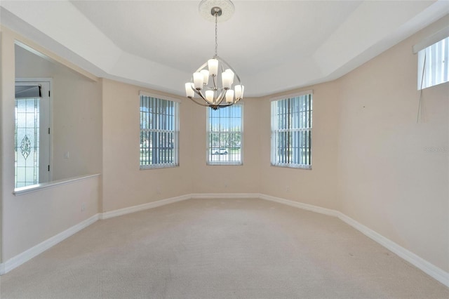 empty room featuring a tray ceiling, carpet flooring, and an inviting chandelier