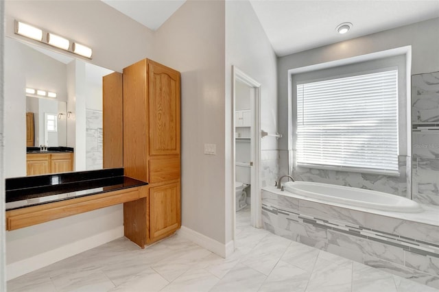 bathroom featuring vanity, a relaxing tiled tub, and toilet