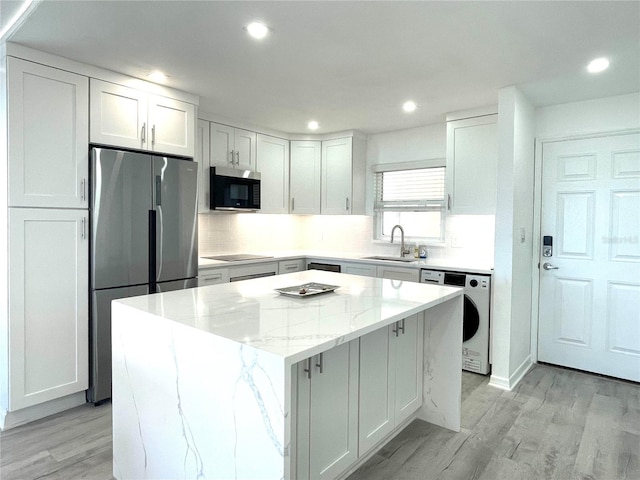 kitchen featuring sink, light stone countertops, appliances with stainless steel finishes, a kitchen island, and washer / clothes dryer