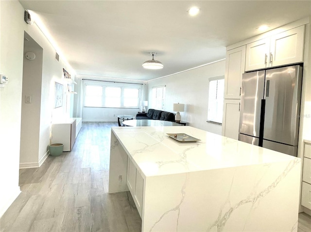 kitchen featuring stainless steel refrigerator, light stone countertops, a center island, light hardwood / wood-style floors, and white cabinets