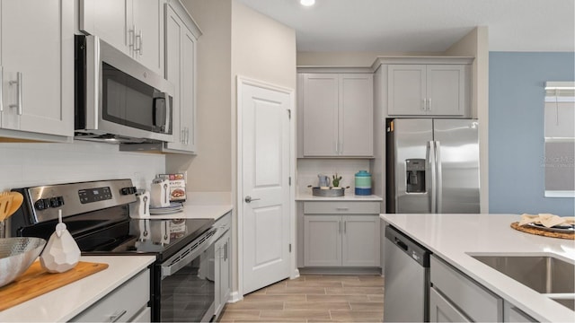 kitchen with appliances with stainless steel finishes, backsplash, light hardwood / wood-style flooring, and gray cabinetry