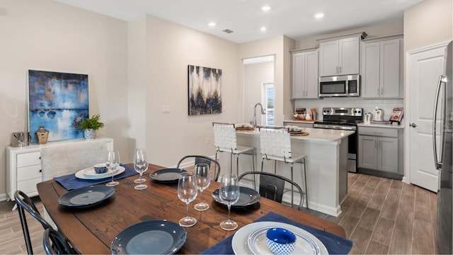 kitchen with gray cabinetry, dark hardwood / wood-style floors, stainless steel appliances, and a kitchen island with sink