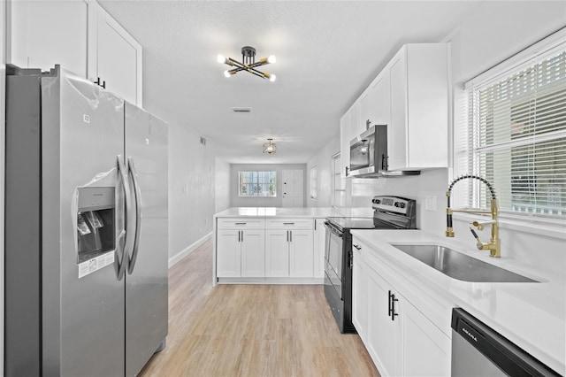 kitchen with sink, light hardwood / wood-style flooring, appliances with stainless steel finishes, white cabinetry, and a chandelier