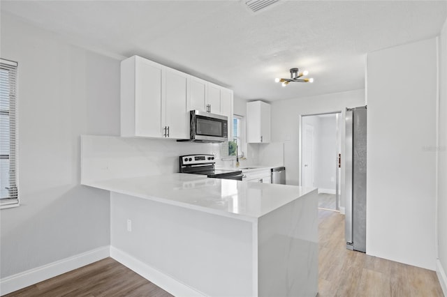 kitchen with white cabinets, light hardwood / wood-style flooring, kitchen peninsula, stainless steel appliances, and a chandelier