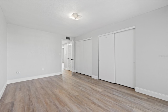 unfurnished bedroom with a textured ceiling, light wood-type flooring, and two closets