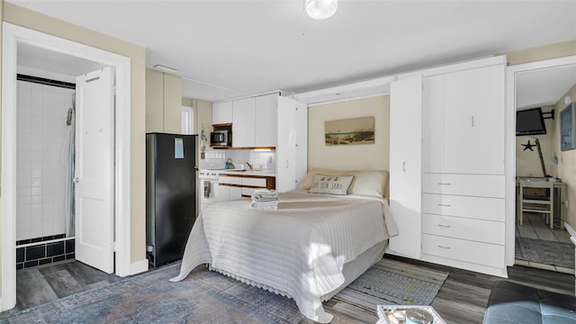 bedroom with ensuite bath, black refrigerator, and dark hardwood / wood-style floors