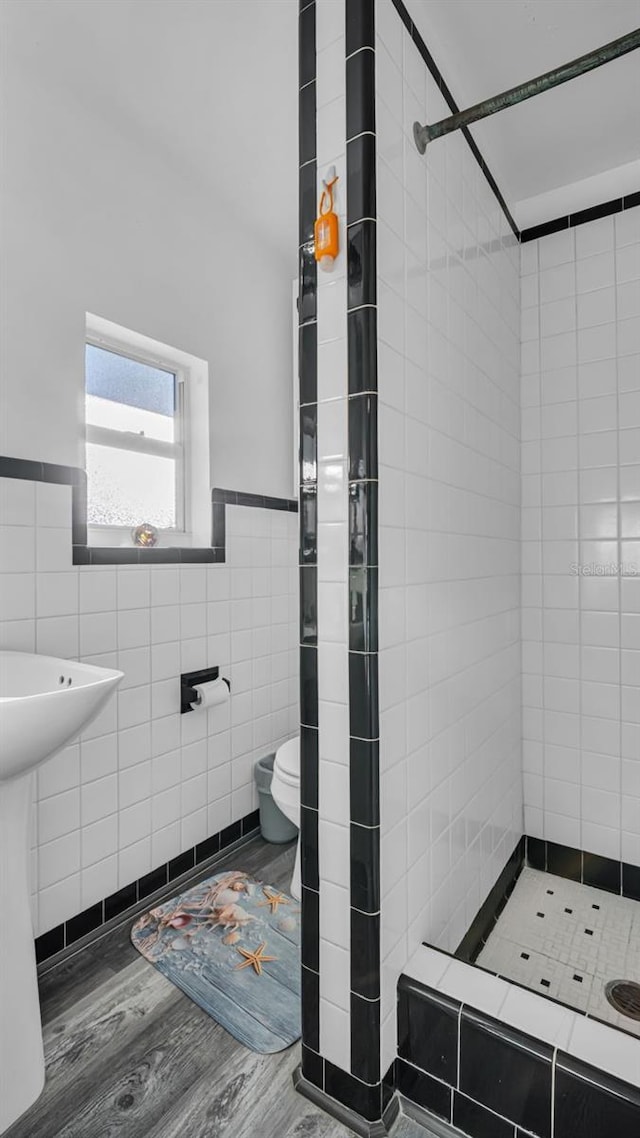 bathroom with tiled shower, hardwood / wood-style floors, toilet, and tile walls