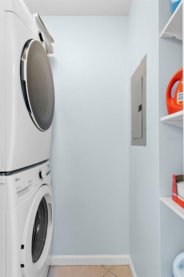 clothes washing area featuring light tile patterned flooring, electric panel, and stacked washer / dryer