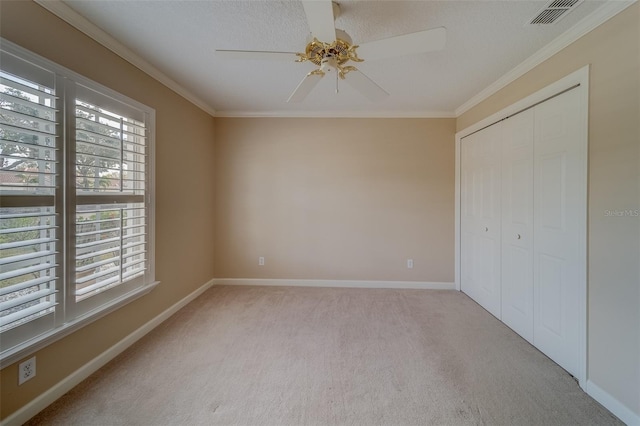 unfurnished bedroom featuring ceiling fan, crown molding, a textured ceiling, light carpet, and a closet