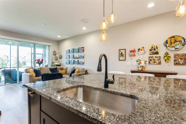 kitchen featuring pendant lighting, sink, dark stone counters, and light hardwood / wood-style flooring