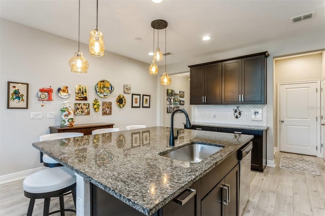 kitchen featuring pendant lighting, sink, an island with sink, dark brown cabinets, and light hardwood / wood-style floors