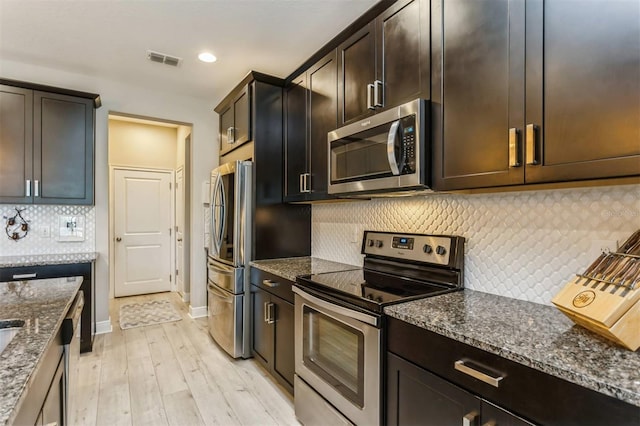 kitchen featuring backsplash, dark stone counters, light hardwood / wood-style floors, and appliances with stainless steel finishes