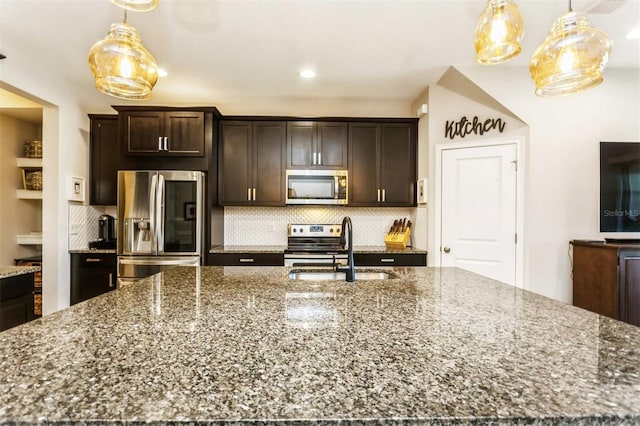 kitchen with appliances with stainless steel finishes, stone countertops, pendant lighting, and sink