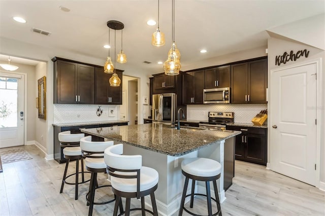 kitchen featuring sink, an island with sink, appliances with stainless steel finishes, decorative light fixtures, and dark brown cabinetry