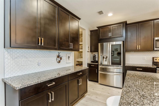 kitchen featuring light stone counters, light wood-type flooring, dark brown cabinetry, and appliances with stainless steel finishes