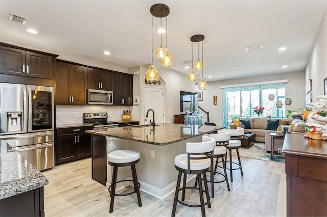 kitchen featuring sink, hanging light fixtures, stainless steel appliances, light hardwood / wood-style flooring, and stone countertops