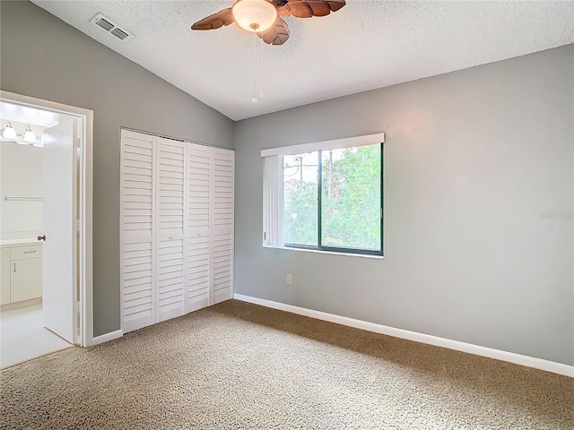 unfurnished bedroom featuring ceiling fan, carpet floors, a textured ceiling, lofted ceiling, and a closet