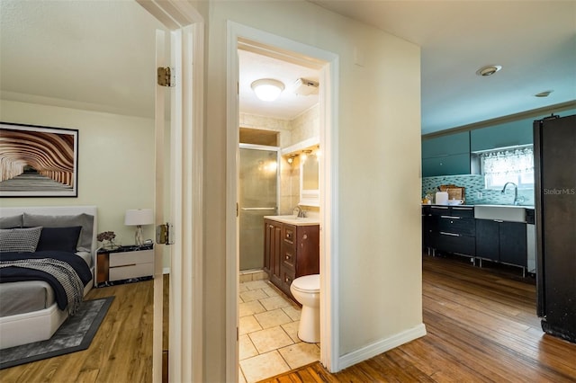 bedroom with black fridge, sink, light wood-type flooring, and ensuite bath